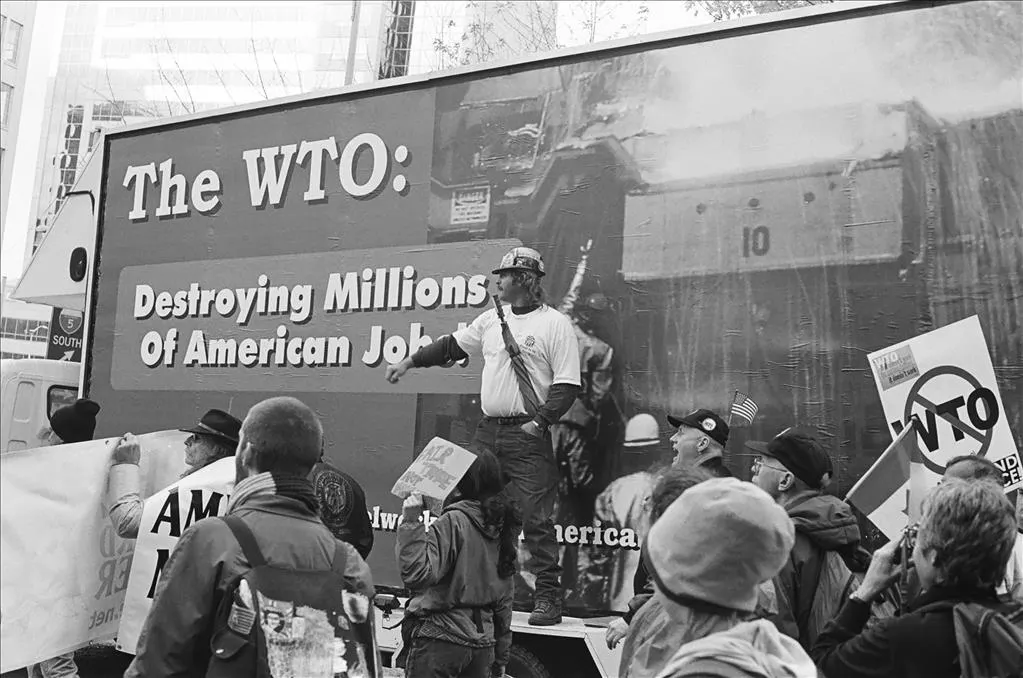 Protesters demonstrating against the WTO in front of a billboard reading The WTO: Destroying Millions of American Jobs